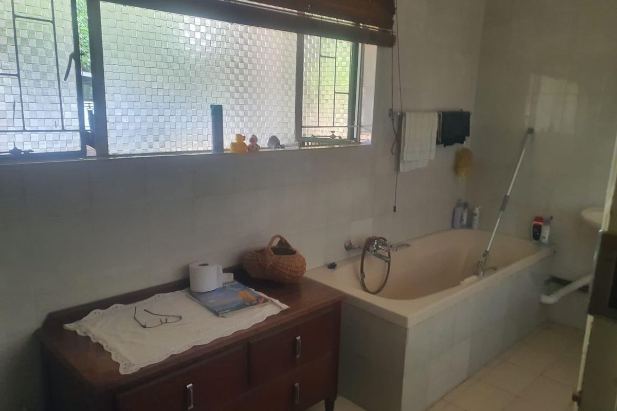 A dated bathroom featuring a built-in bathtub, tiled walls, and a large window with security bars.