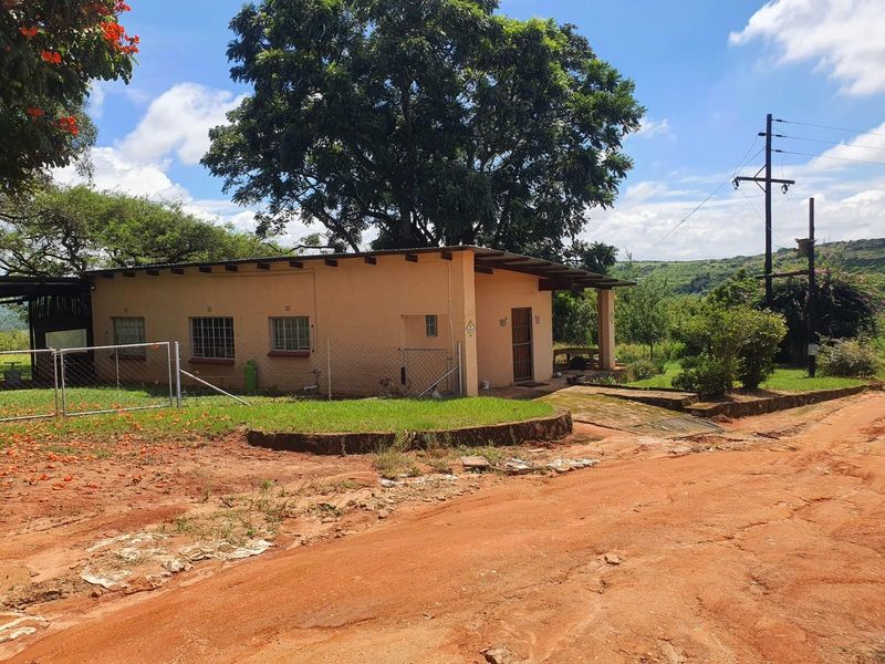 A modest single-story farm dwelling featuring a corrugated metal roof, security bars on windows, and a surrounding rural landscape.
