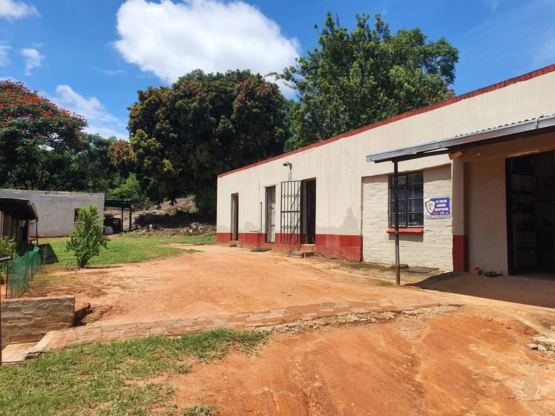 Exterior view of a farm building featuring a dirt driveway, simple masonry construction, and a covered entrance area.