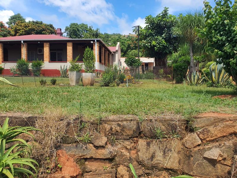 A view of the farm property featuring a covered patio, brick pillars, and a landscaped garden with a natural stone retaining wall.