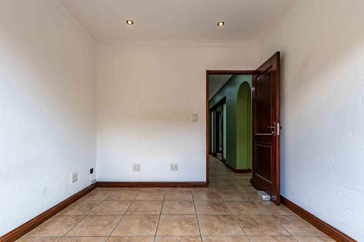 An empty bedroom featuring tiled flooring, recessed ceiling lighting, and a wooden door leading to a hallway.