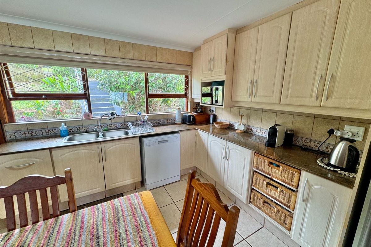 A functional kitchen featuring light-toned cabinetry, granite countertops, a double basin sink, and tiled flooring with a view of the garden.