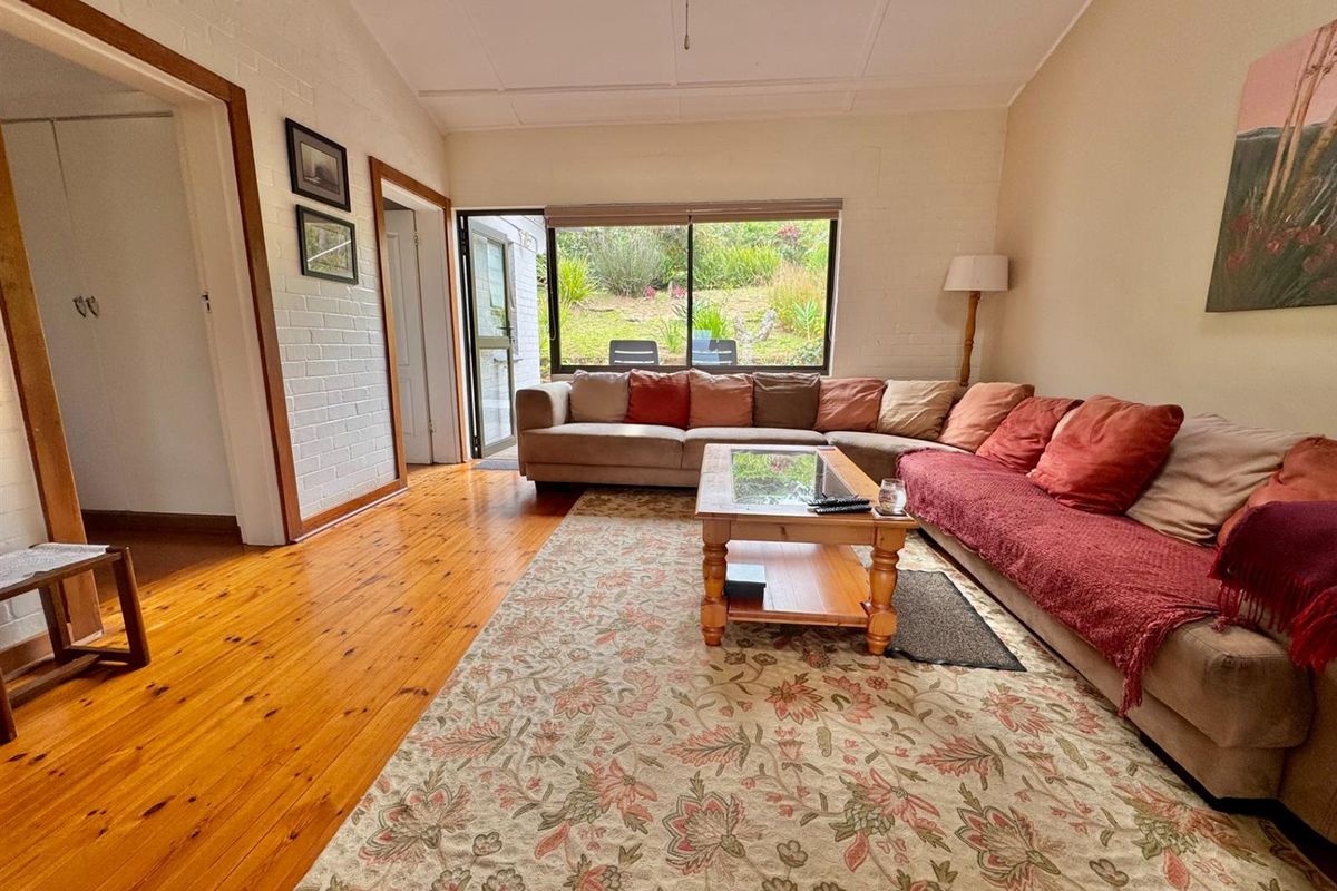 A comfortable living room featuring polished timber flooring, painted brick walls, and large windows providing natural light and garden views.