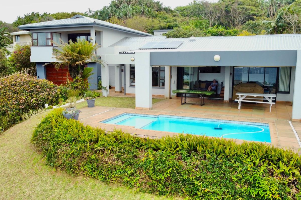 An elevated view of the rear exterior featuring a covered patio, swimming pool, and landscaped garden area with solar panels on the roof.
