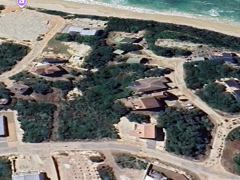 An aerial view of a coastal residential area featuring vacant land plots and established homes near the beach.