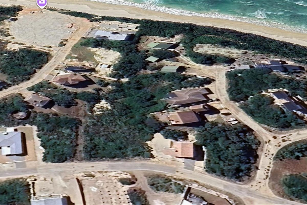 An aerial view of a coastal residential area featuring vacant land plots and established homes near the beach.