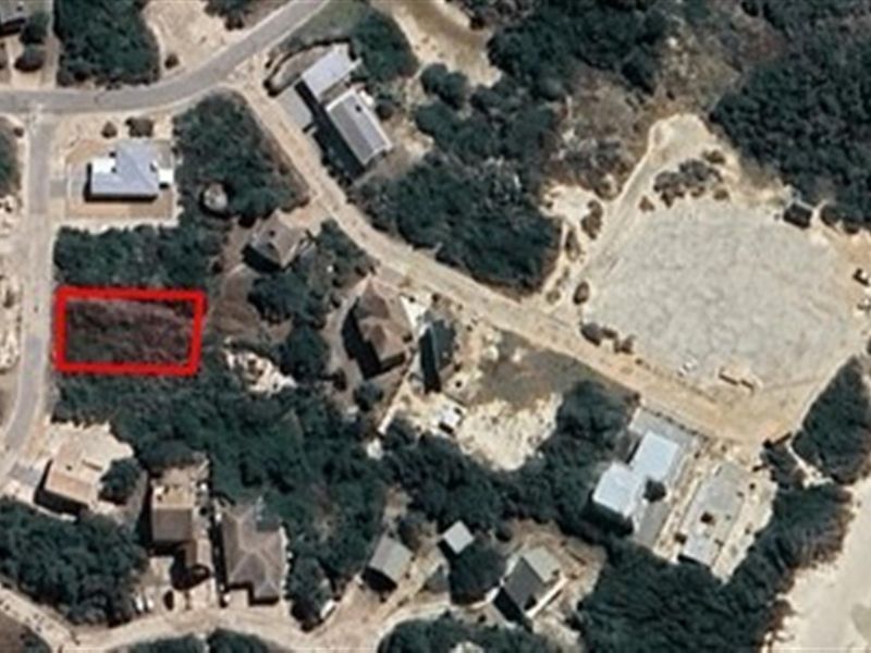 Aerial view of a vacant residential plot highlighted in red, situated within a coastal neighborhood setting.