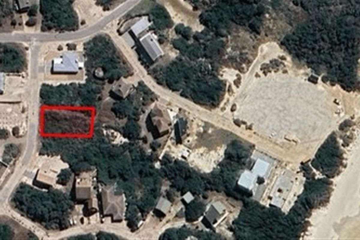 Aerial view of a vacant residential plot highlighted in red, situated within a coastal neighborhood setting.