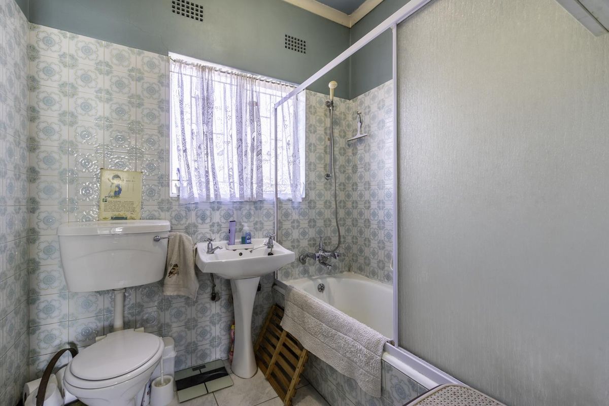 A dated bathroom featuring a pedestal basin, toilet, and a shower-over-bath combination with original patterned wall tiles.
