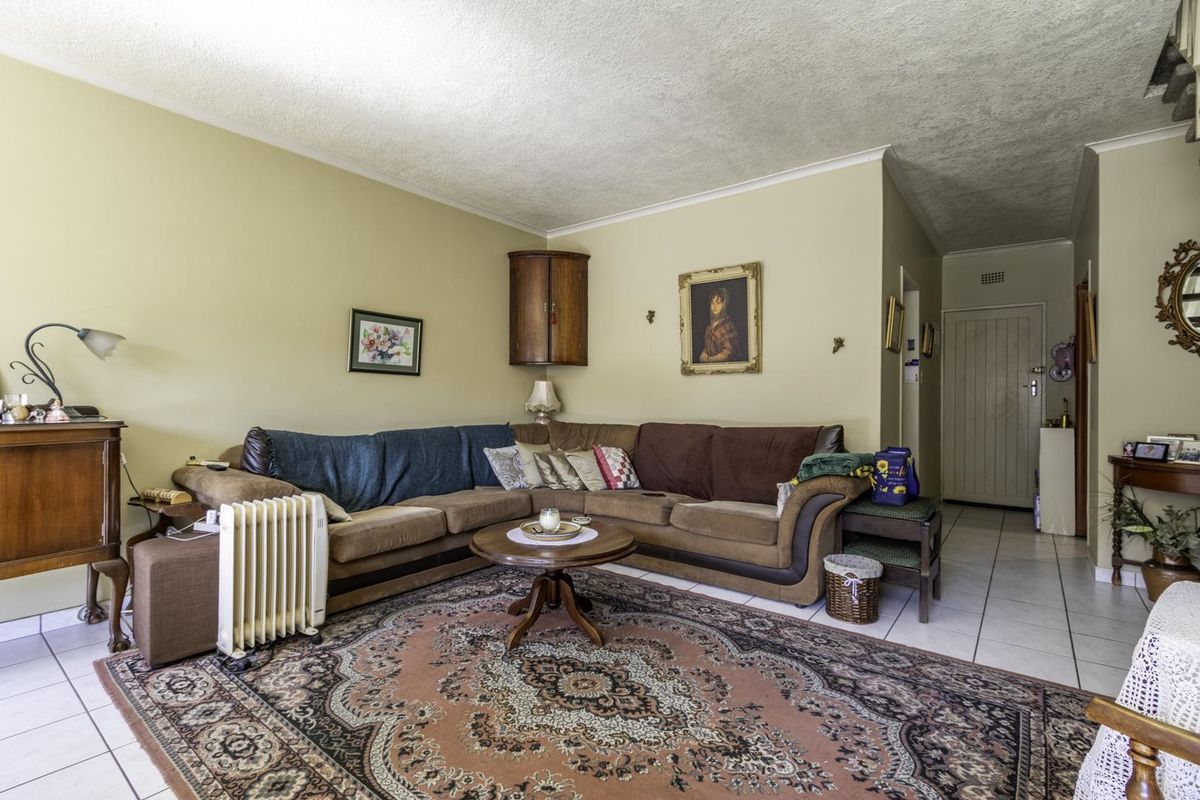 A living room featuring tiled flooring, a corner wall cabinet, and access to the entrance hallway.