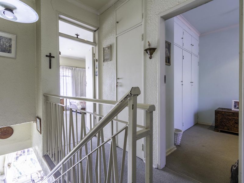 A landing area featuring a staircase railing, built-in storage cupboards, and access to adjacent rooms with dated finishes.