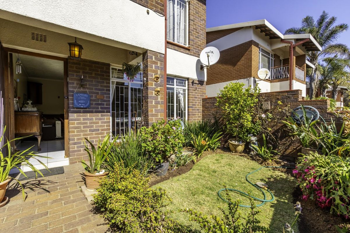 A well-maintained rear townhouse exterior featuring a paved patio area, landscaped garden, and brick facade with security features.