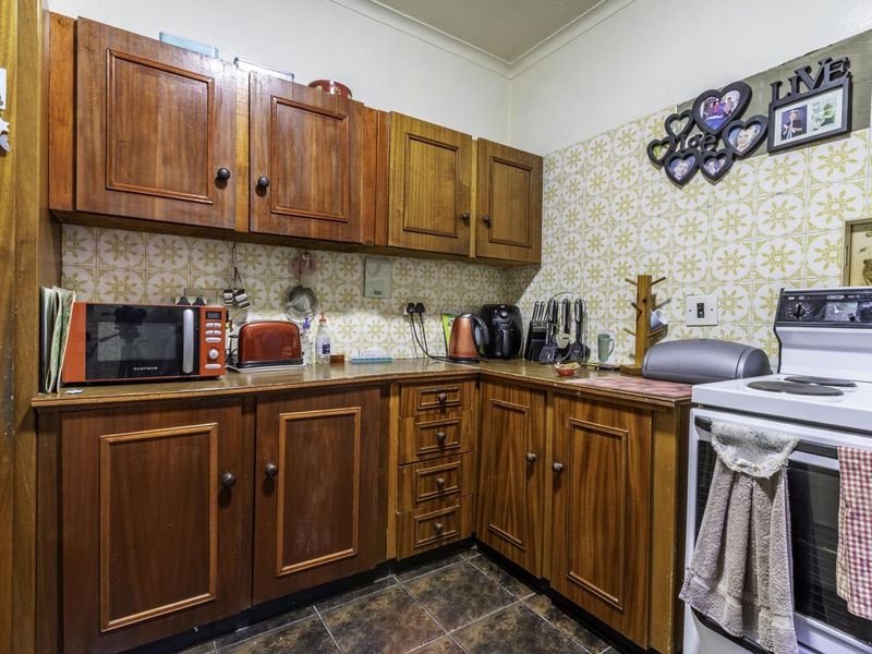 A compact kitchen featuring traditional wooden cabinetry, patterned tiled backsplash, and durable tiled flooring, offering a functional layout with potential for modern updates.