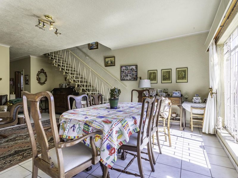 Open plan living and dining area featuring tiled flooring and a prominent staircase with a metal balustrade, offering a functional layout.
