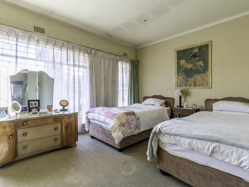 A spacious bedroom featuring large windows with natural light, carpeted flooring, and coved ceilings, offering a blank canvas for modernization and renovation.