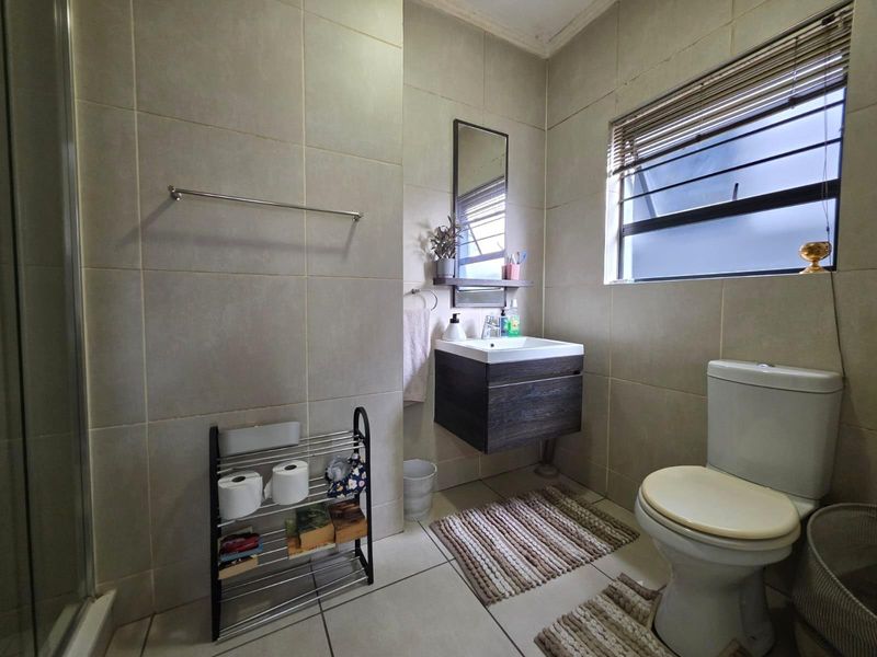 A functional bathroom featuring a wall-mounted vanity, ceramic toilet, and a shower enclosure with neutral wall and floor tiling.