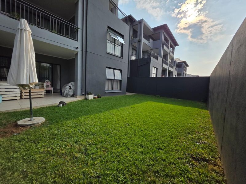 A private rear garden featuring a well-maintained lawn, a tiled patio area, and modern dark-toned apartment building architecture.