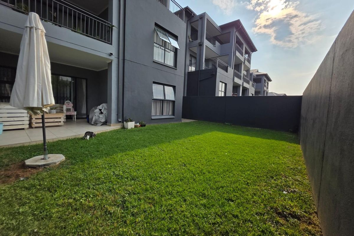 A private rear garden featuring a well-maintained lawn, a tiled patio area, and modern dark-toned apartment building architecture.