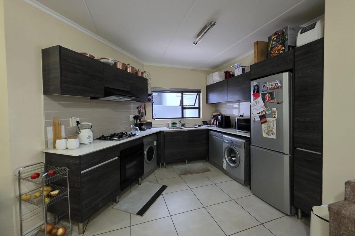 A functional kitchen featuring dark wood-grain cabinetry, a gas hob, built-in oven, extractor fan, and integrated space for laundry appliances.