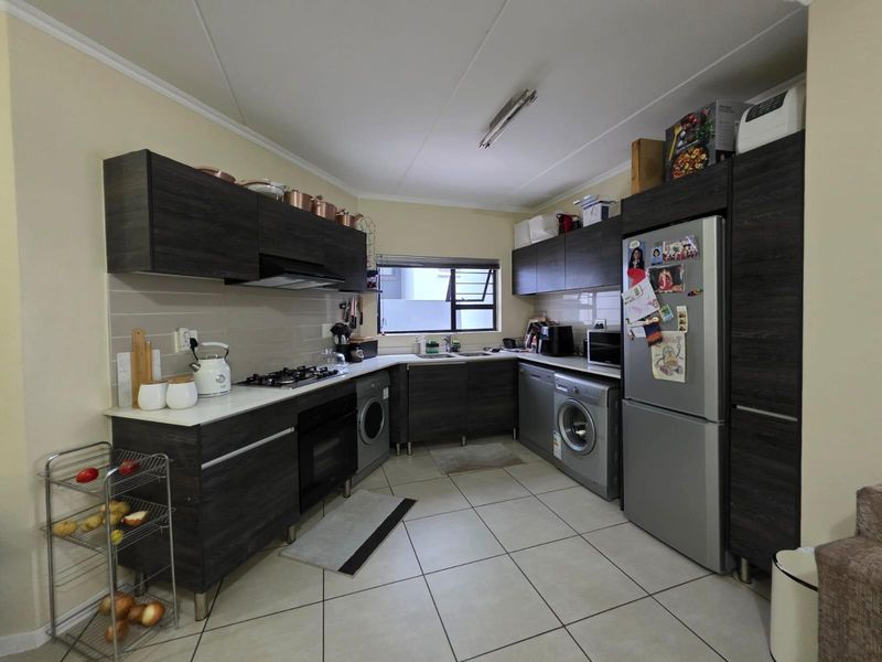 A functional kitchen featuring dark wood-grain cabinetry, a gas hob, built-in oven, extractor fan, and integrated space for laundry appliances.