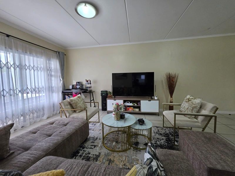 A well-lit living room featuring tiled flooring and a large sliding glass door with an integrated security gate, providing access to the exterior.