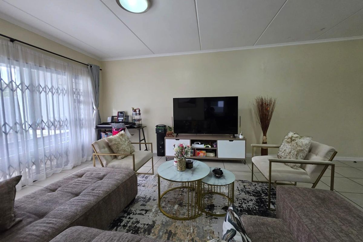 A well-lit living room featuring tiled flooring and a large sliding glass door with an integrated security gate, providing access to the exterior.