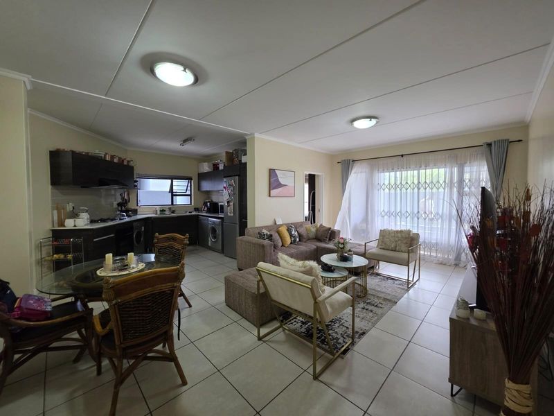 Open-plan living and kitchen area featuring tiled flooring, modern cabinetry, and a sliding door leading to an outdoor space with security gate.