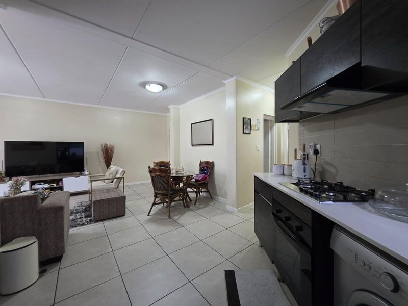 Open-plan living area featuring a modern kitchen with dark cabinetry, gas hob, and tiled flooring, seamlessly flowing into the dining and lounge space.