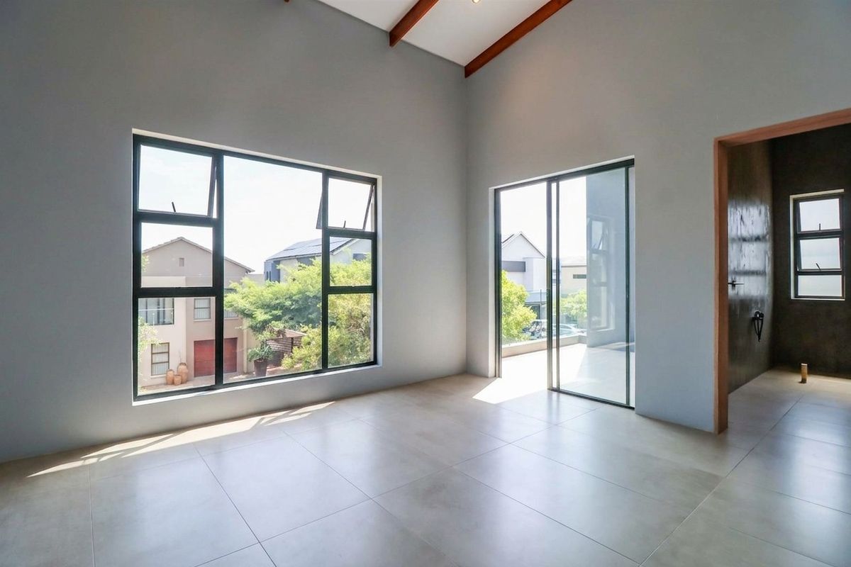 Spacious, light-filled bedroom featuring vaulted ceilings with exposed timber beams, large windows, and modern tiled flooring, offering a clean and contemporary aesthetic.