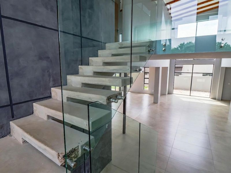 Modern double-volume entrance hall featuring a striking concrete staircase with glass balustrades and large format floor tiles in an open-plan layout.