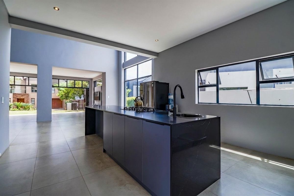 Modern open-plan kitchen featuring a sleek black island with integrated gas hob, undermount sink, and high-quality stone countertops in a bright, contemporary space.