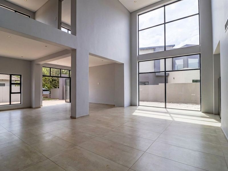 Spacious open-plan living area featuring double-volume ceilings, large windows for natural light, and modern tiled flooring in a contemporary architectural design.