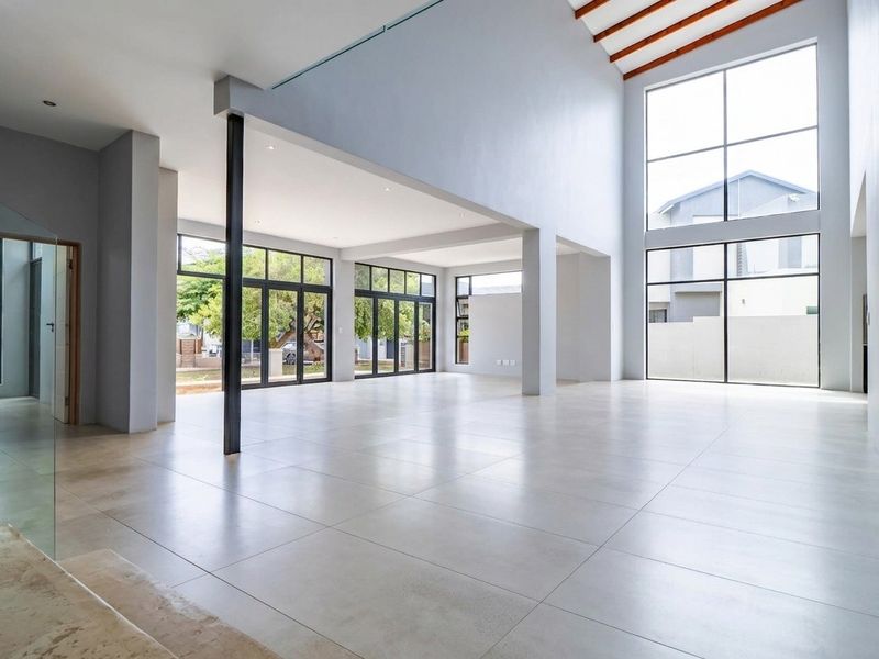 Spacious open-plan living area featuring double-volume ceilings, exposed timber rafters, large format floor tiles, and expansive aluminium-framed windows providing abundant natural light.