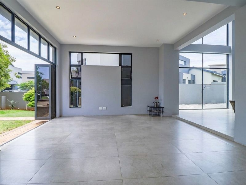 Spacious, modern open-plan living area featuring large format floor tiles, recessed lighting, and expansive aluminium-framed glass doors opening to the garden.
