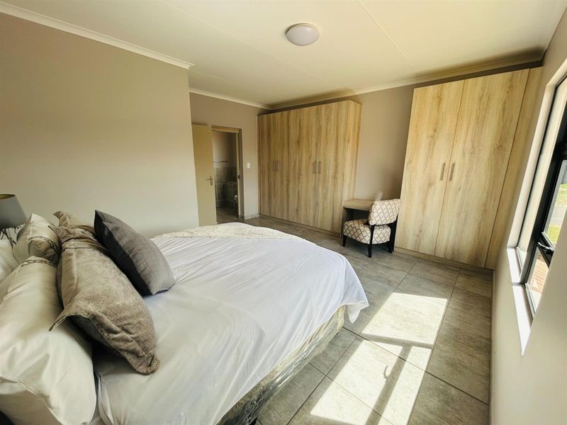 A well-lit bedroom featuring built-in wooden wardrobes, tiled flooring, and an en-suite bathroom entrance.