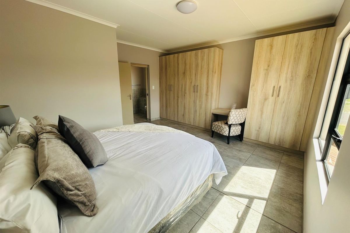 A well-lit bedroom featuring built-in wooden wardrobes, tiled flooring, and an en-suite bathroom entrance.