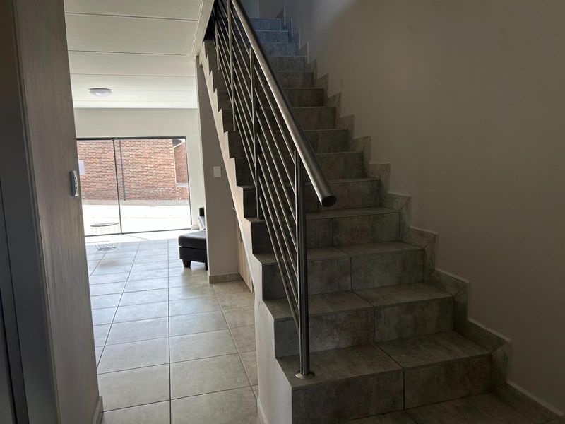 Interior view of a tiled hallway featuring a staircase with a modern stainless steel balustrade, leading towards an open-plan living area with sliding doors.