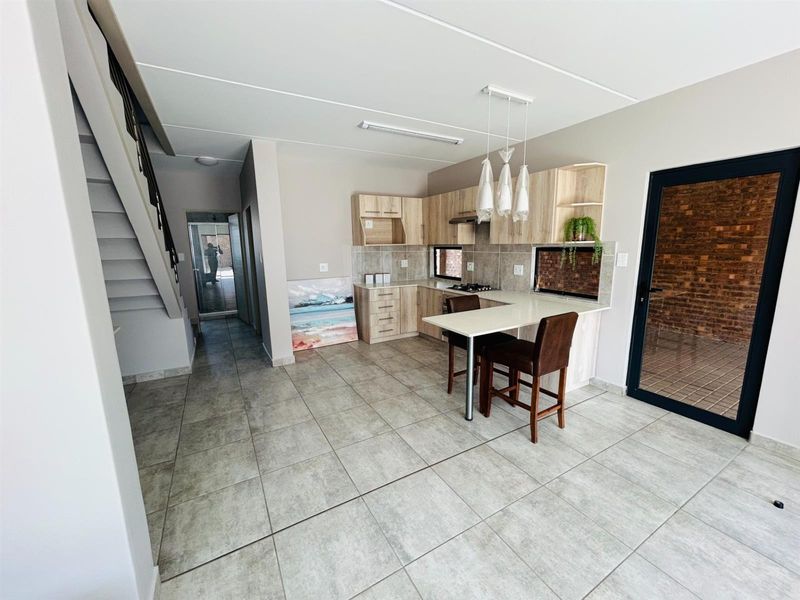 Open-plan kitchen featuring light wood cabinetry, integrated breakfast bar, tiled flooring, and direct access to an outdoor area via a glass door.