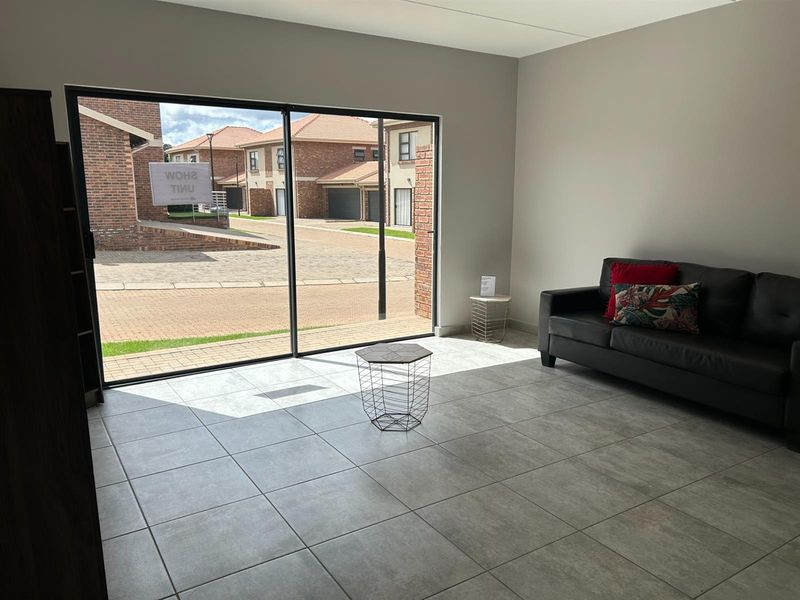 A bright living room featuring large sliding glass doors that open to a paved exterior area, finished with neutral floor tiles.