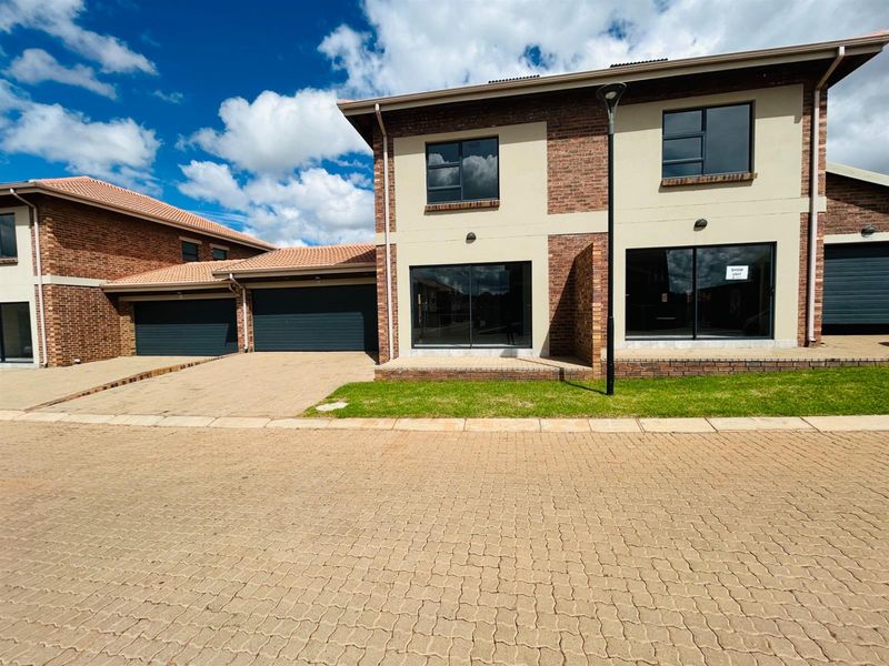 A modern double-storey townhouse exterior featuring brick and plaster facade, tiled roof, paved driveway, and integrated double garage.