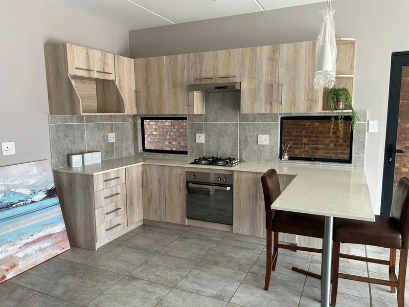Modern kitchen featuring light wood-grain cabinetry, stone countertops, a built-in gas hob, oven, extractor fan, and a breakfast bar.