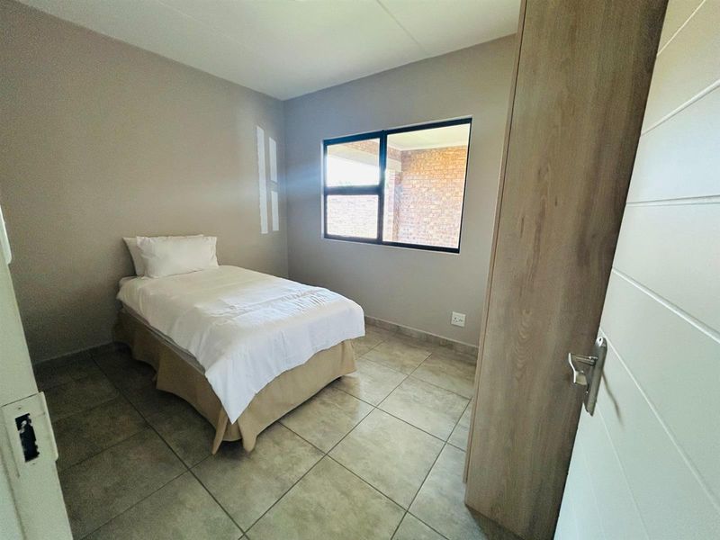 A bedroom featuring tiled flooring, a built-in wardrobe, and a window overlooking an exterior brick wall.