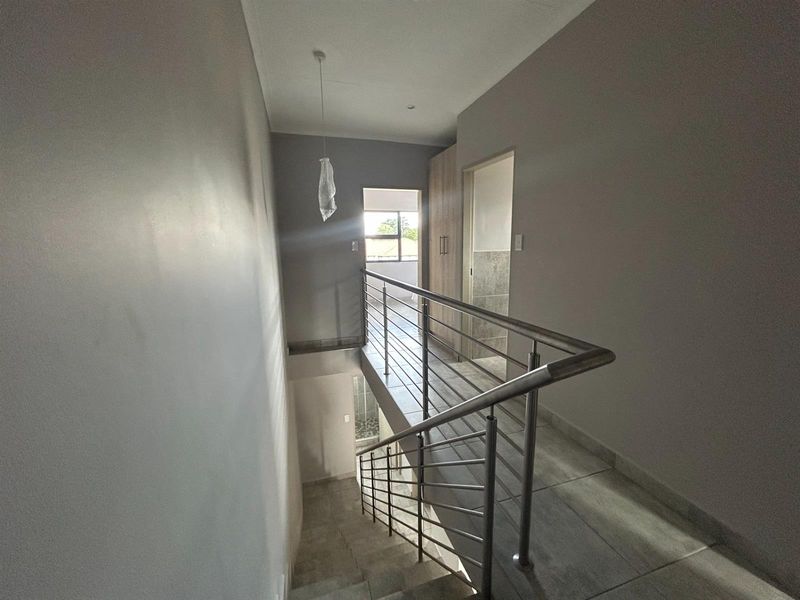 A bright upstairs landing area featuring modern tiled flooring and a sleek stainless steel balustrade overlooking the staircase.