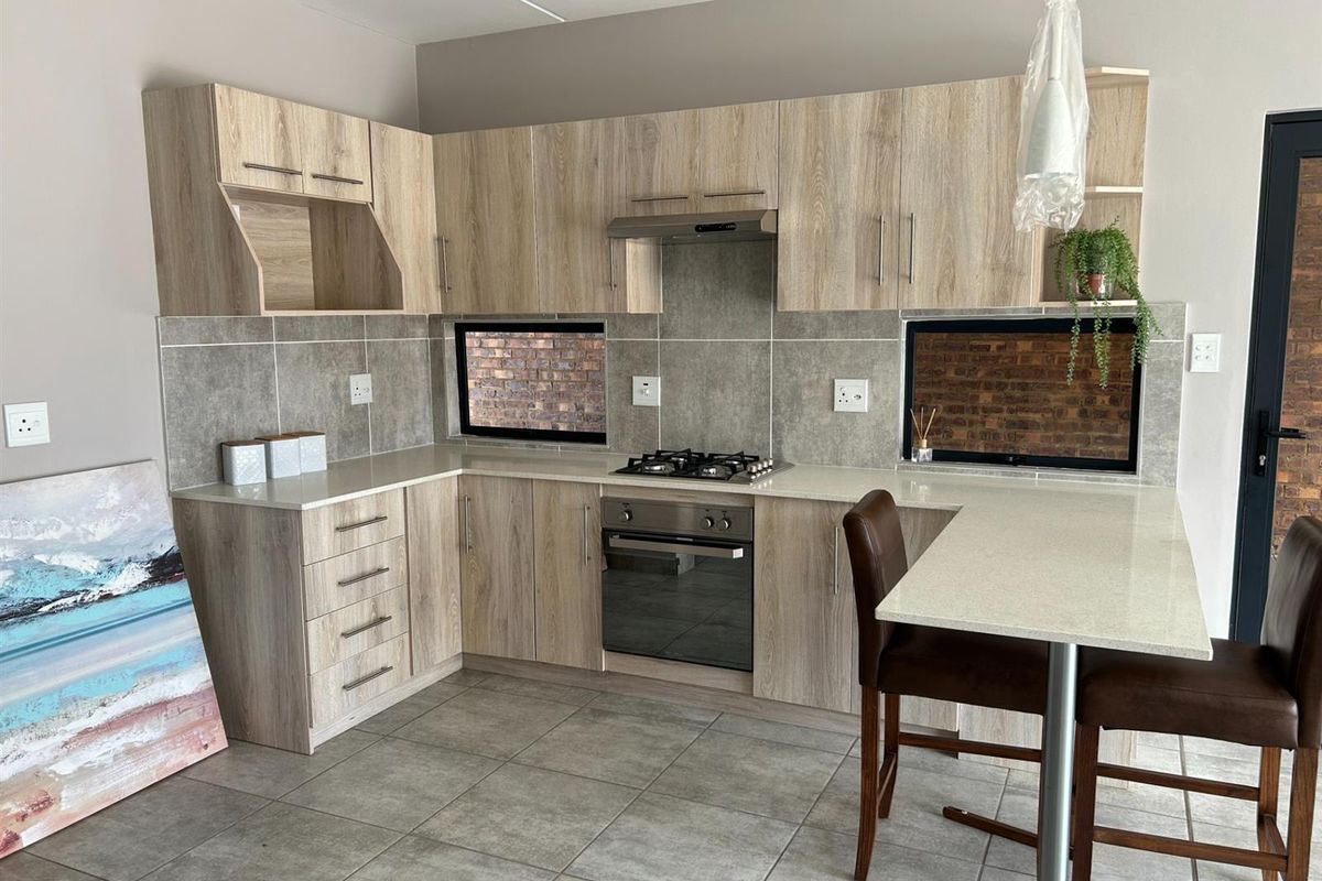 Modern kitchen featuring light wood-grain cabinetry, stone countertops, a built-in gas hob, oven, extractor fan, and a breakfast bar.