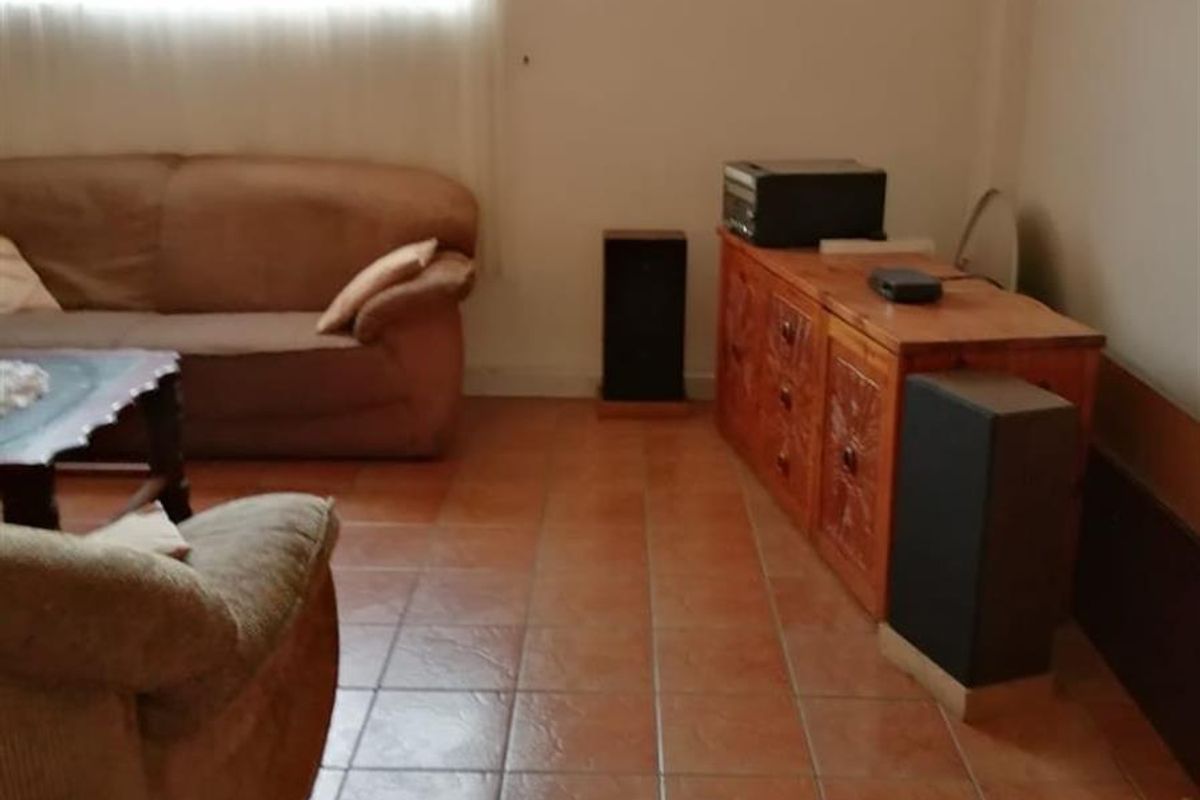 A living room featuring terracotta floor tiles and a large window with sheer curtains.