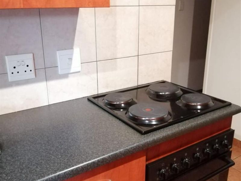 A functional kitchen area featuring wooden cabinetry, a dark countertop, and a built-in electric stove with a four-plate hob.