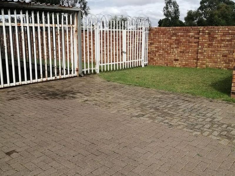 A secure outdoor area featuring paved driveway space, a lawn, and perimeter brick walling with white metal security gates and razor wire.