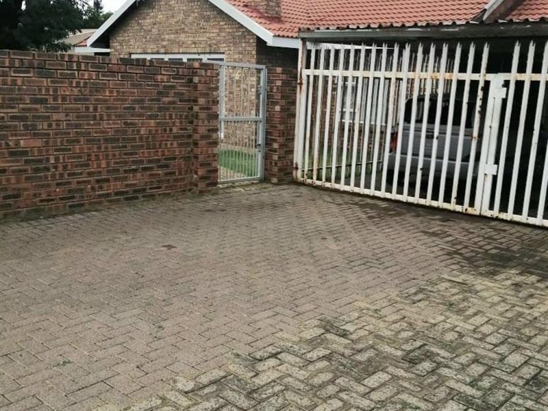 Front exterior view of the property featuring a brick facade, tiled roof, paved driveway, and secure metal gate entrance.