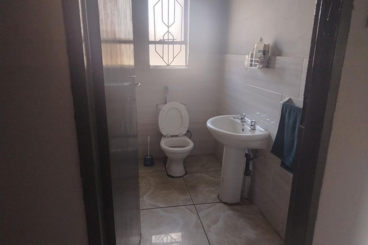 A functional bathroom featuring a pedestal basin, toilet, and tiled flooring with a window providing natural light.