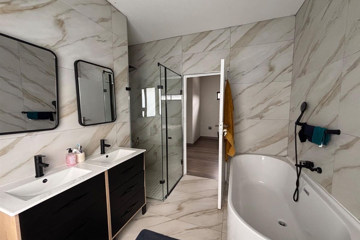 Modern bathroom featuring a double vanity with black cabinetry, a walk-in glass shower, and a sleek freestanding bathtub with contemporary black fixtures.